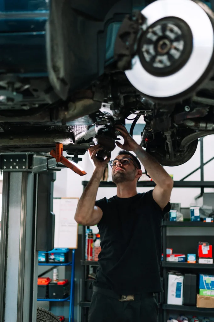 Auto repair technician using power tools under a lifted car in a body shopAuto repair technician using power tools under a lifted car in a body shop